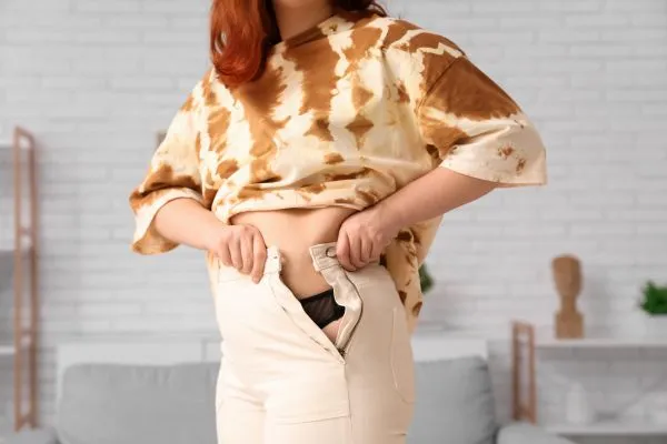 Image of woman trying to do her trousers up after pregnancy weight gain Hertford