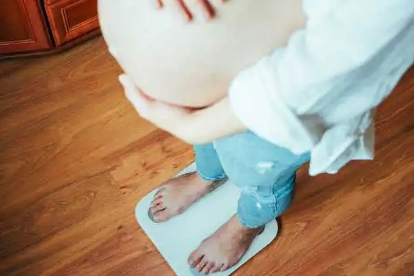 Image of woman weighing herself and experiencing weight gain through pregnancy Hertford